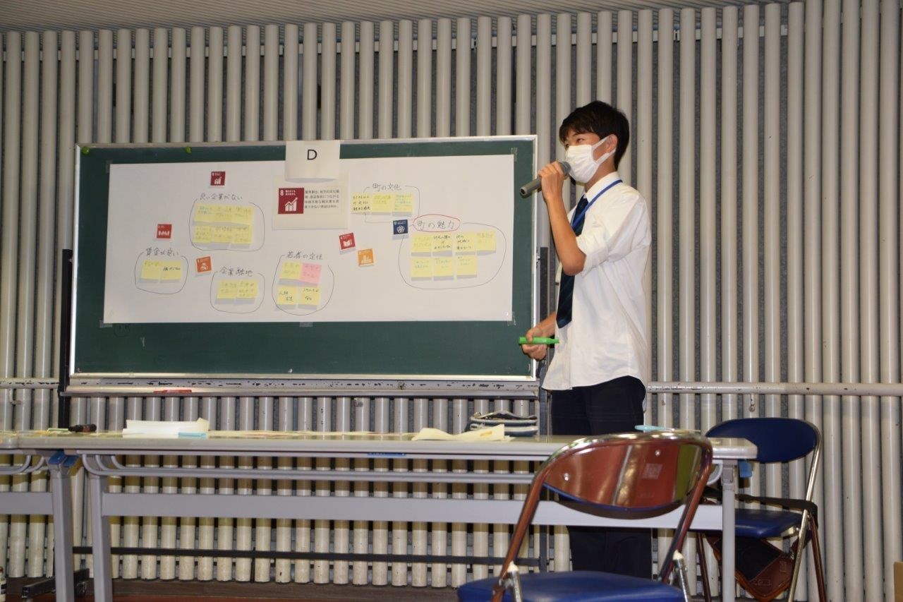 資料を張った黒板を見せながら話をするマスクをした男性の写真