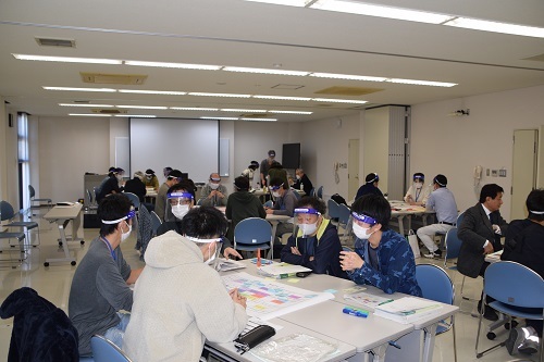 明るい室内でグループごとに机を囲んで話し合う人たちの写真