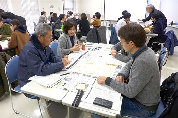 大きな机に資料を広げて話し合う人たちの写真