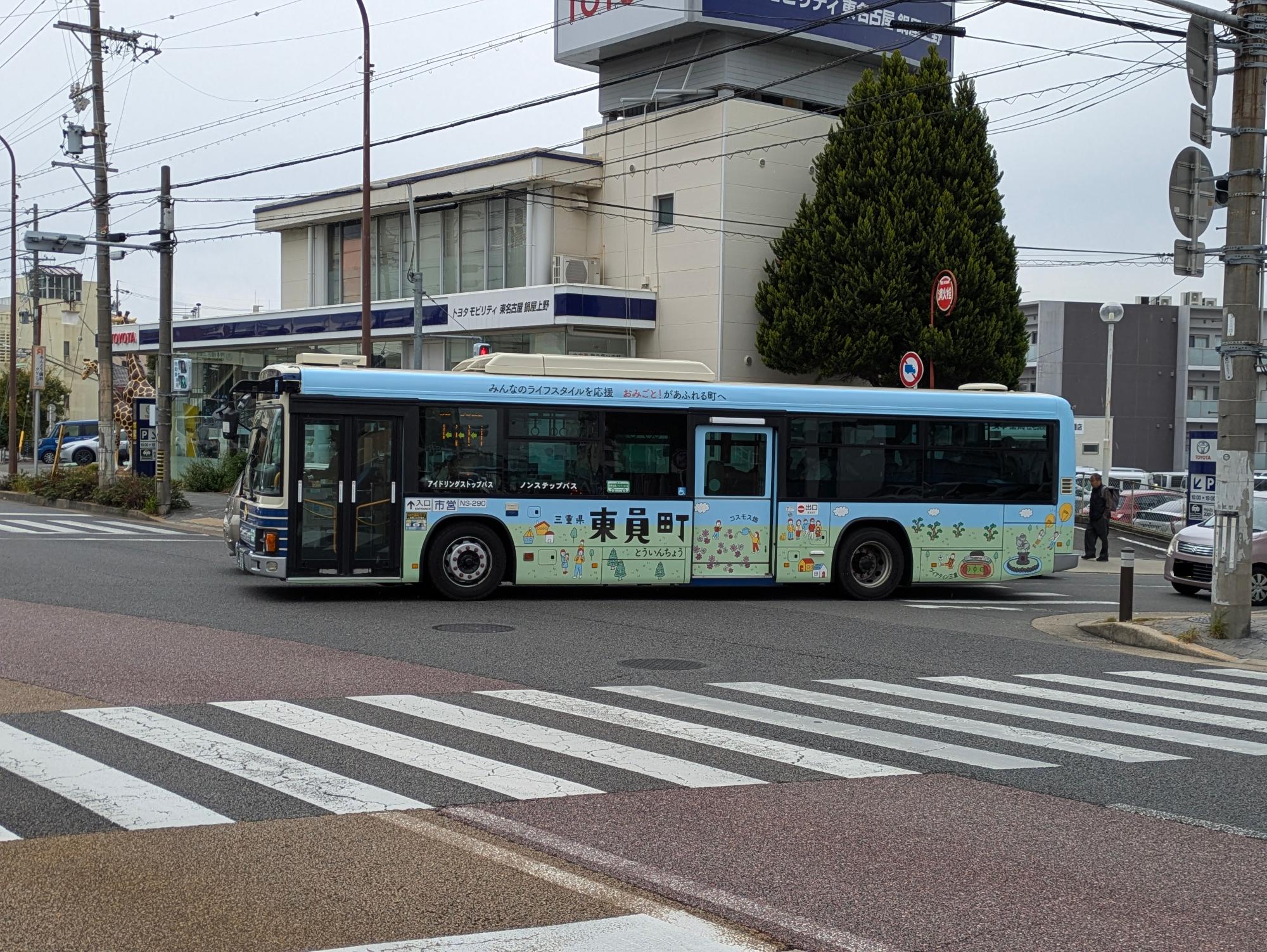 名古屋市大森営業所系統を走行する水色を基調とした東員町ポスターデザインにラッピングした名古屋市バスが交差点を右折する様子をアップで撮影した画像