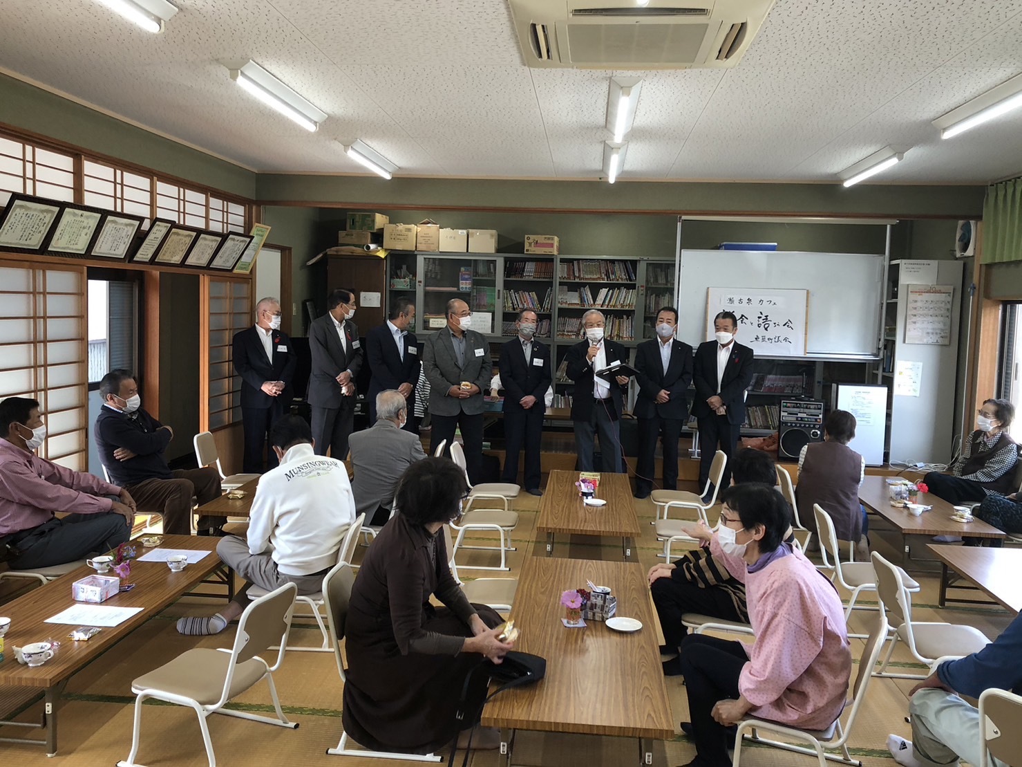 瀬古泉カフェで町民たちを前に横一列に並び挨拶をしている議員たちの写真