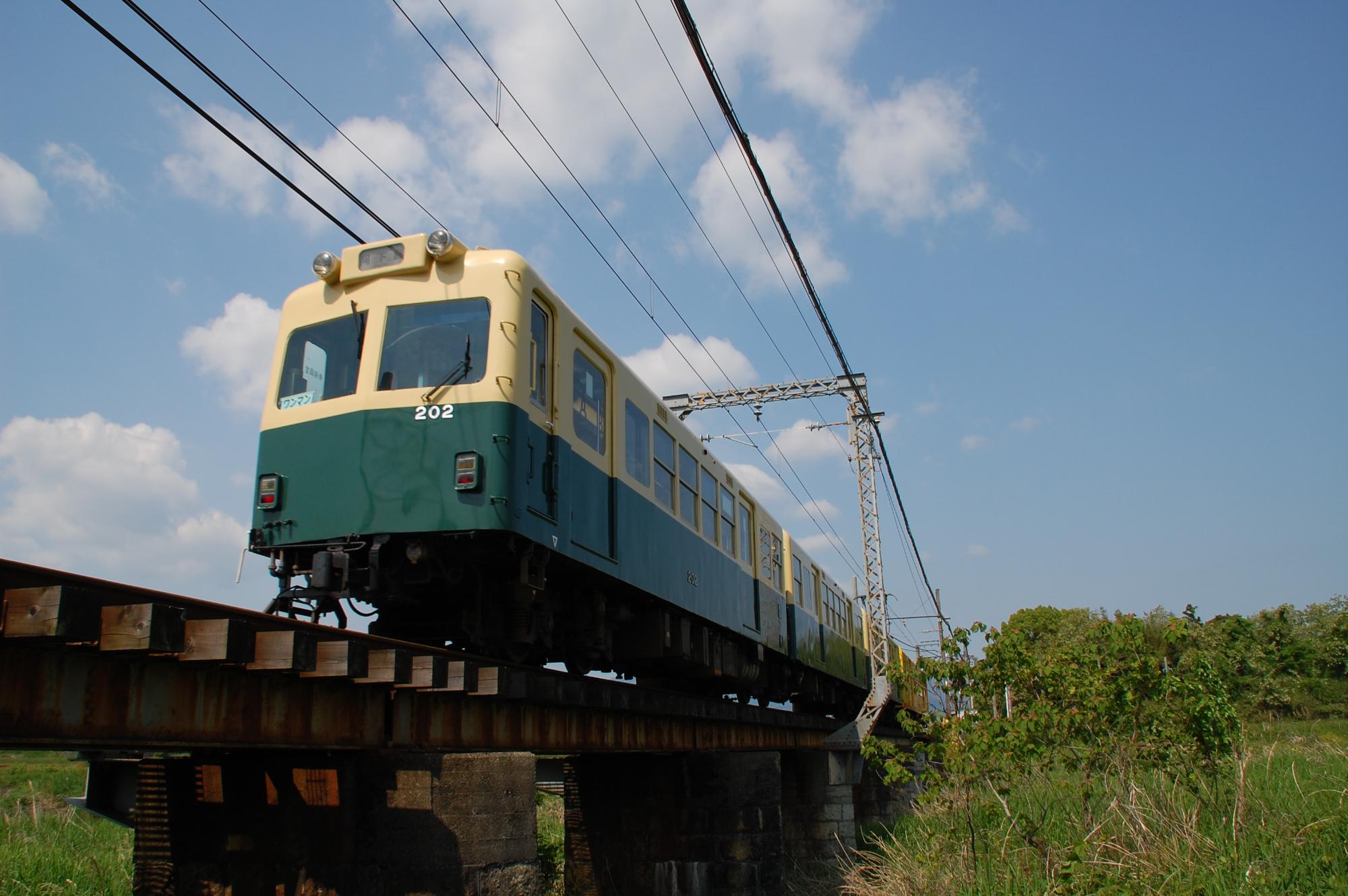 陸橋を渡るクリーム色と緑色の車体の列車の写真