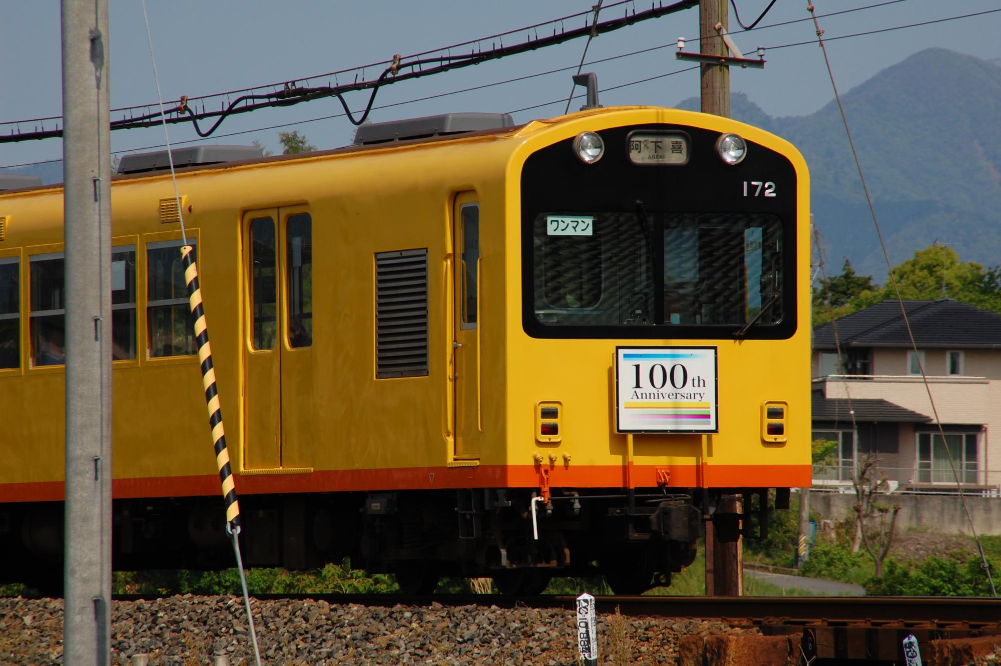 100周年のヘッドマークをつけて走る黄色にオレンジのラインの列車の写真