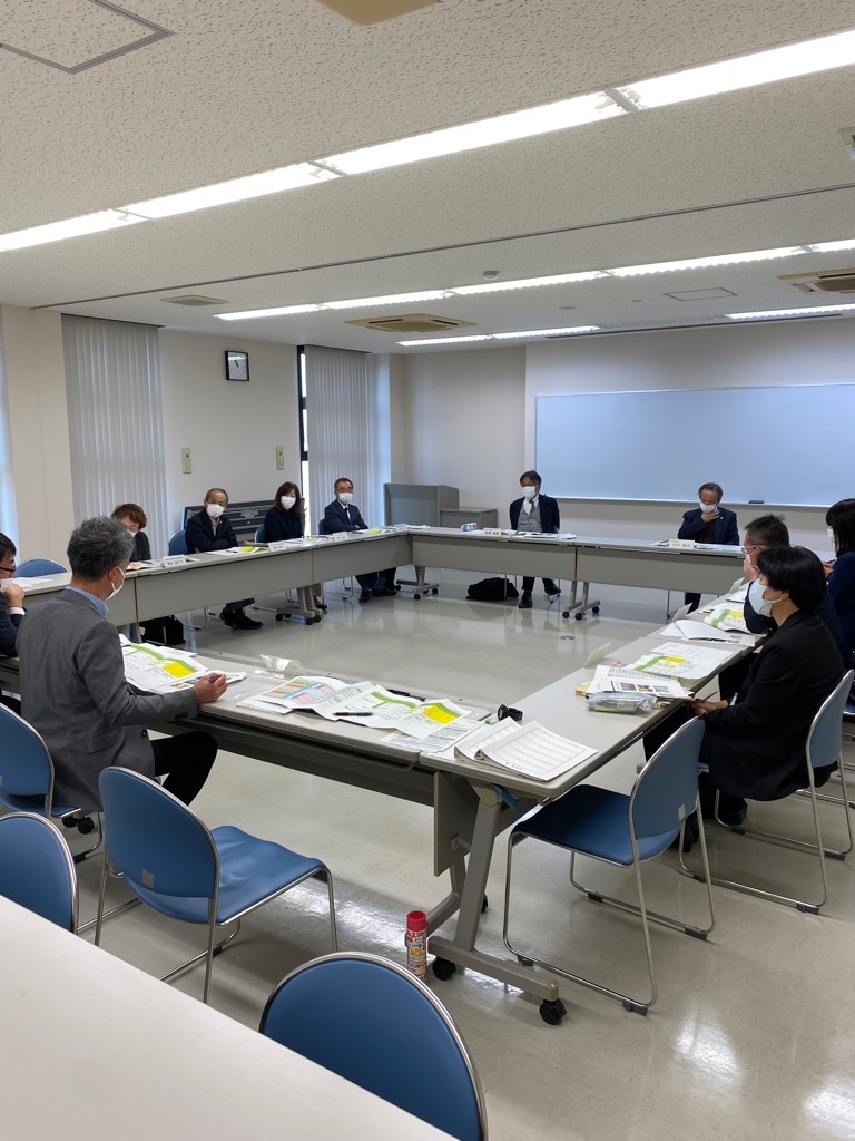 四角く並べた机の上に資料をひろげて会議をする人たちの写真