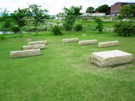 庭木のある芝生に長方形型の石が7つ置かれている園地の写真