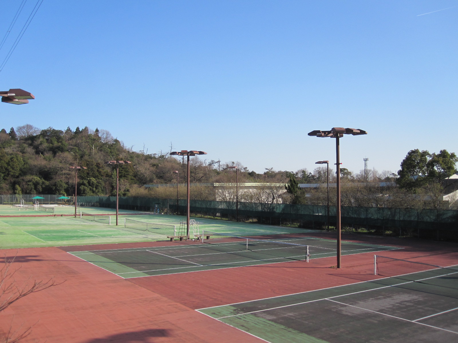 青空の下に木々と緑のコートが並ぶ城山テニスコート