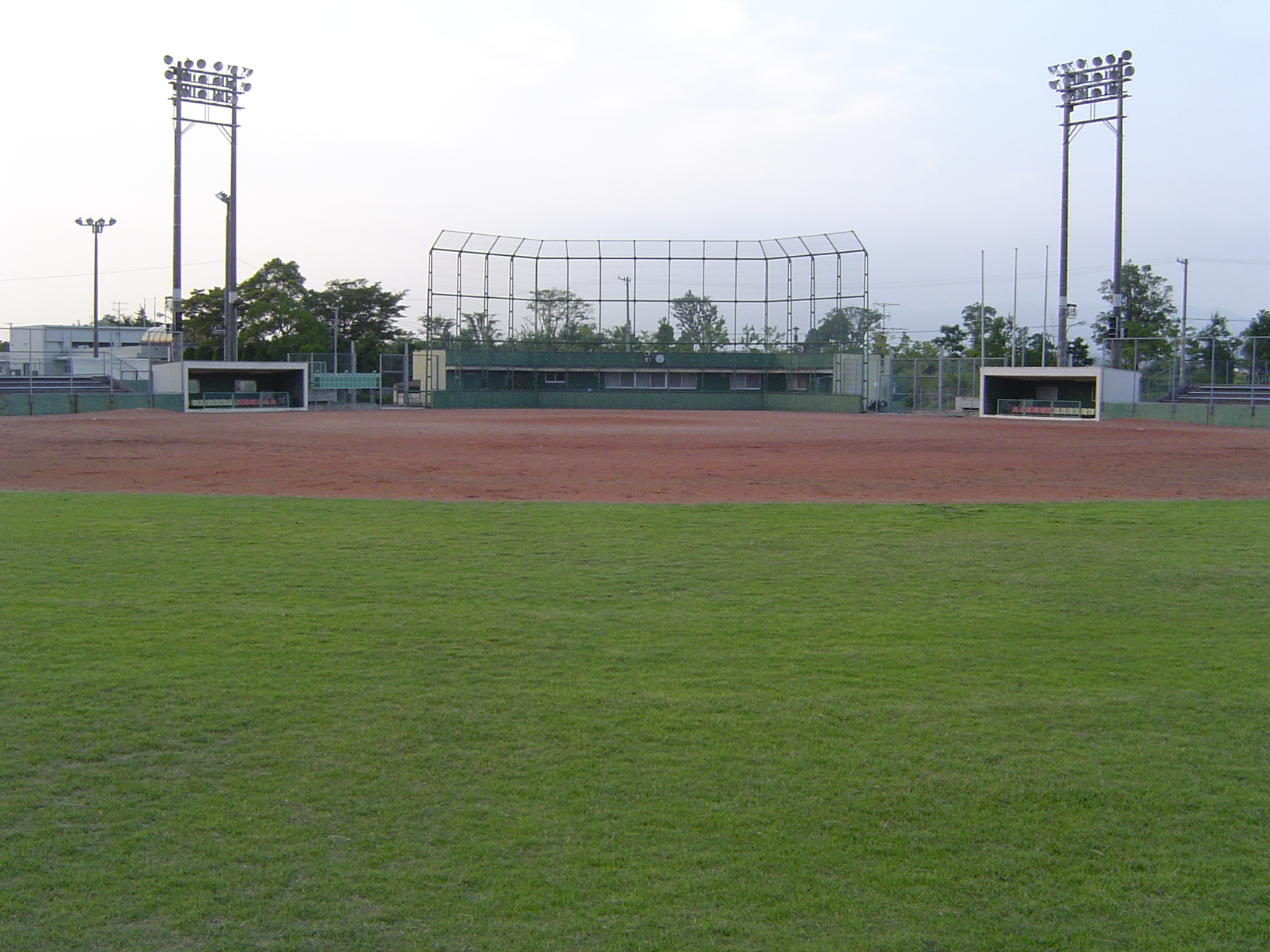 中央にバックネットがありその両サイドに両軍ベンチがありその上には照明が写っている東員町中央球場の写真
