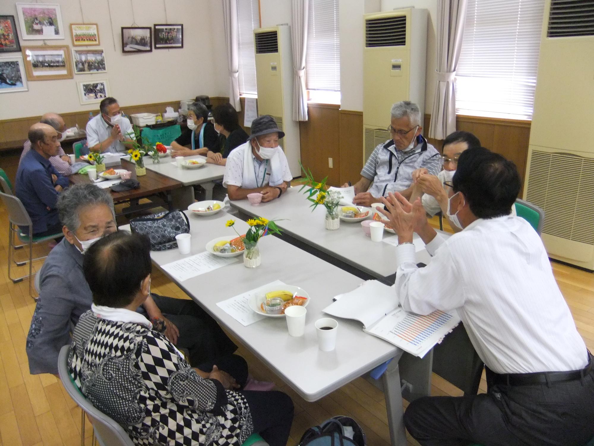 テーブルで資料を拡げ説明している議員と聞き入る町民の写真