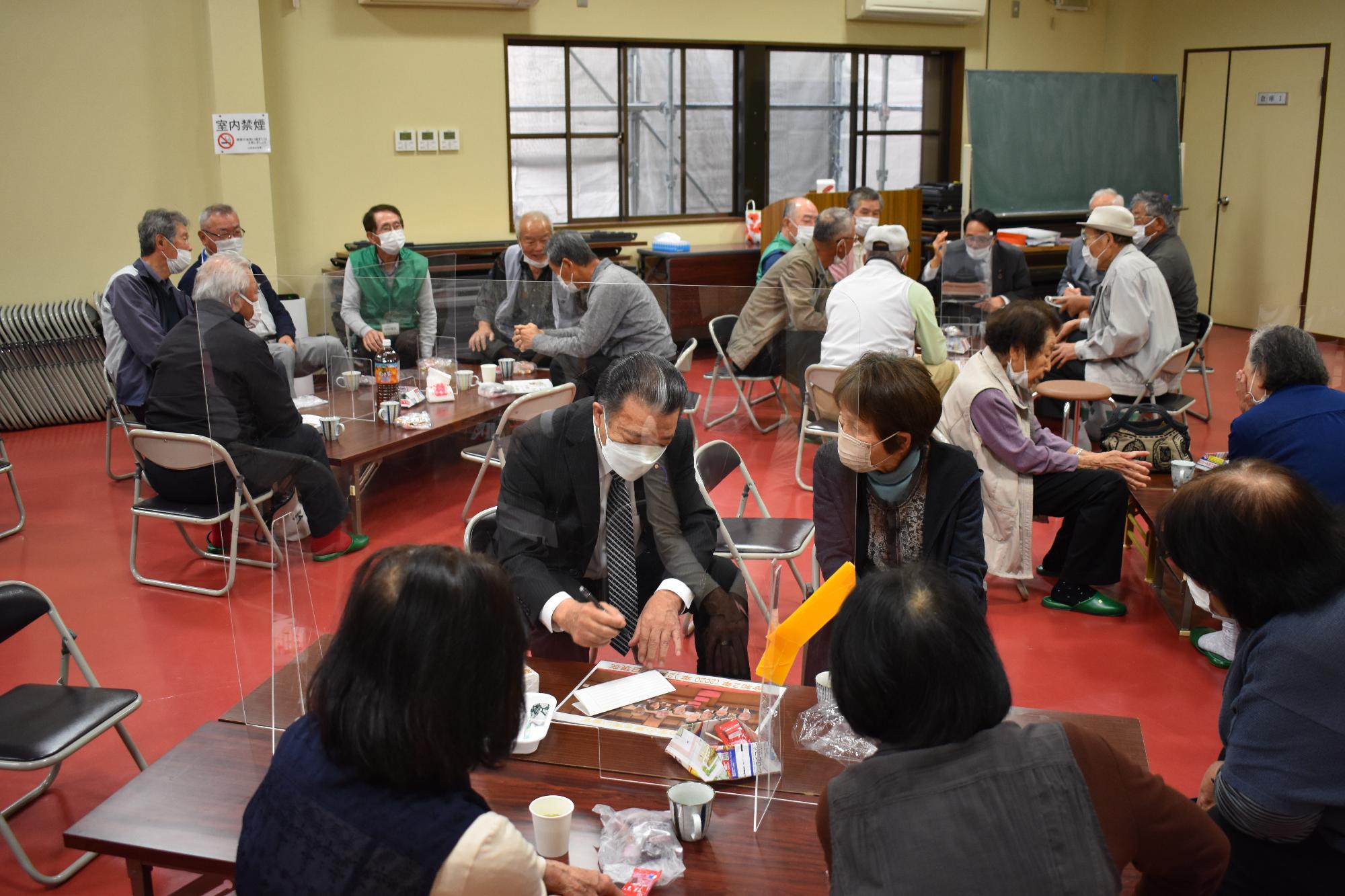 書きながら説明をする議員と聞きいる町民、身振り手振りで説明する議員の話を聞く町民たちの写真