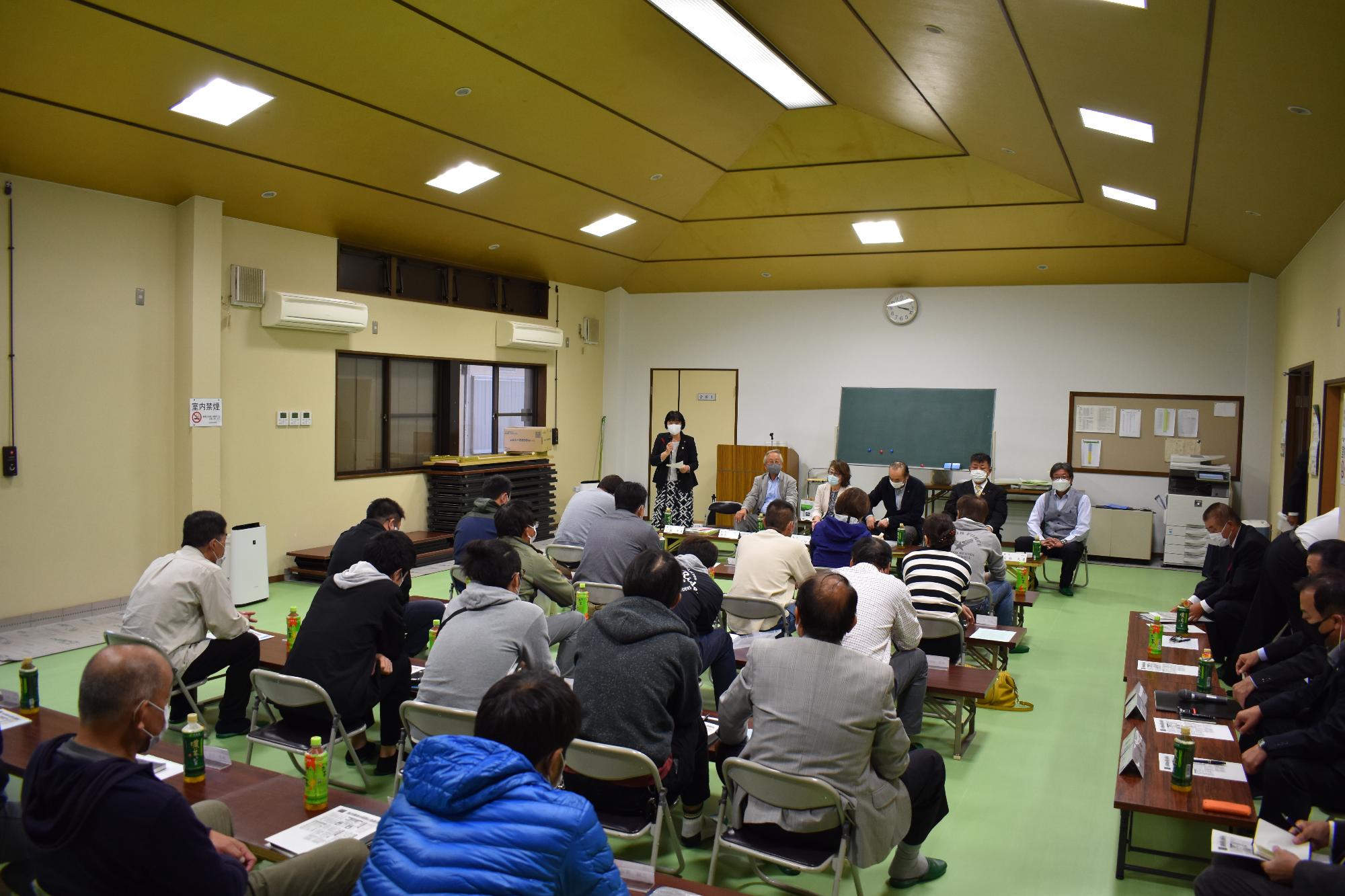 山田自治会で立って説明する議員と真剣に聞き入る町民の写真