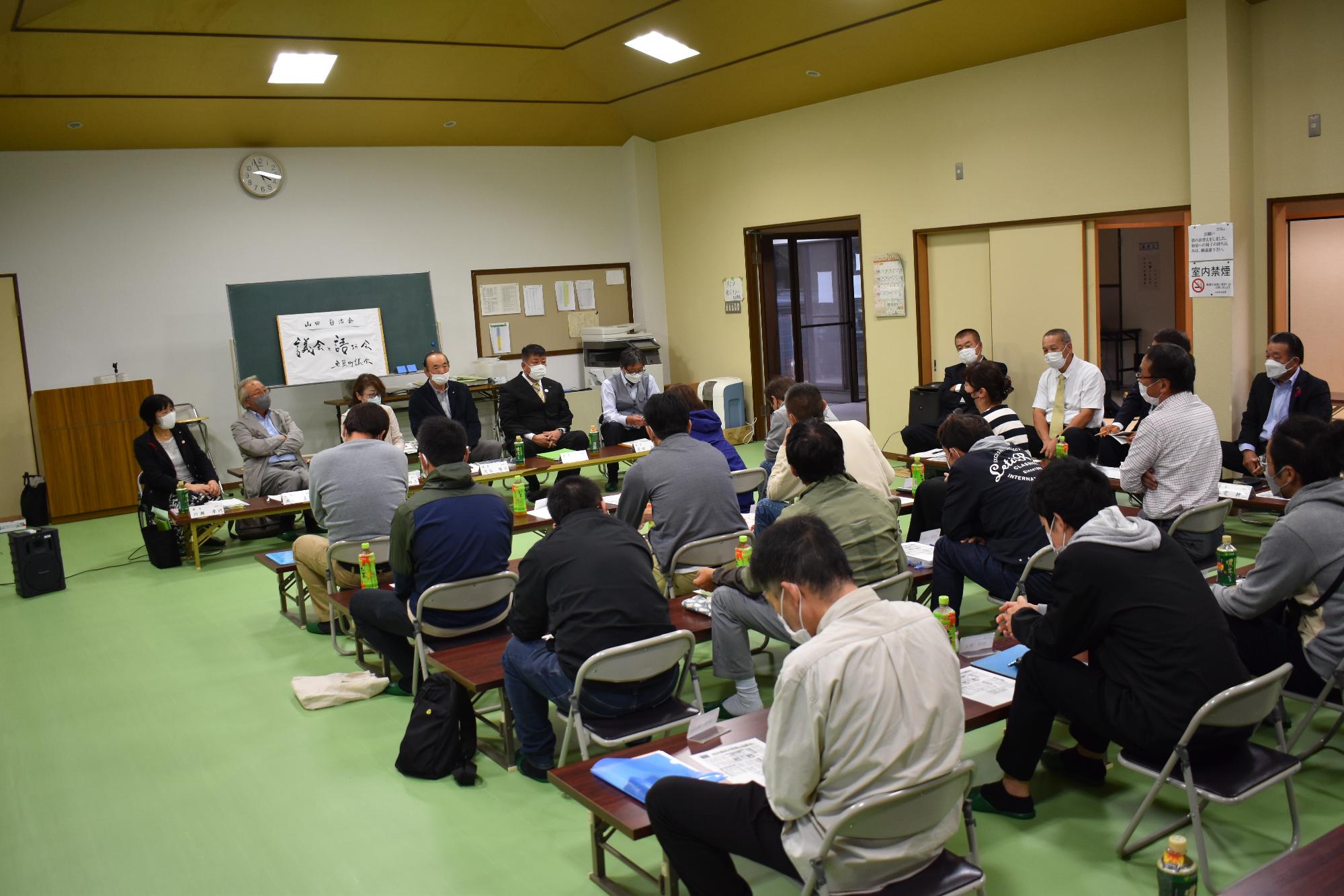 山田自治会の会場で正面に議員たちが横一列に座って説明している写真