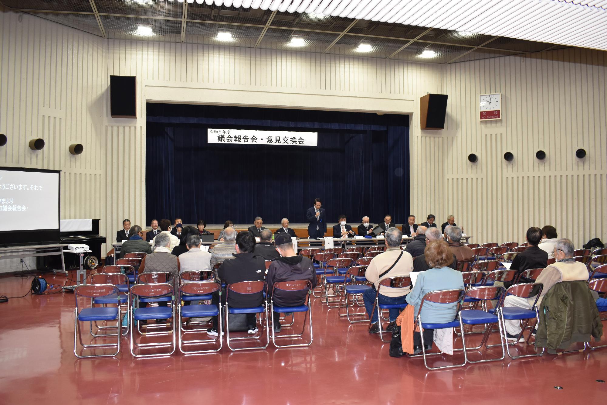 正面に議員たちが座り後ろに町民が座って議会報告を受けている写真